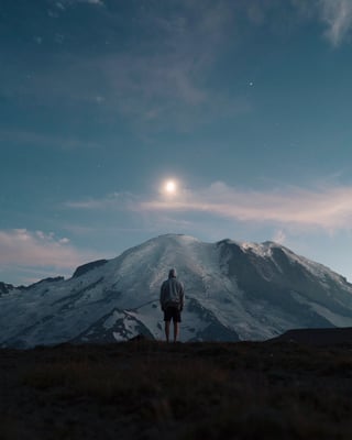 man staring at moon over snowy mountail