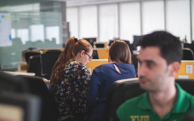 two women talking at a desk, man sitting in front