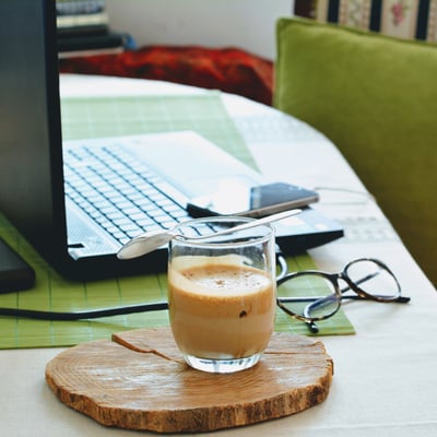 half drunk coffee in front of laptop and green chair and glasses