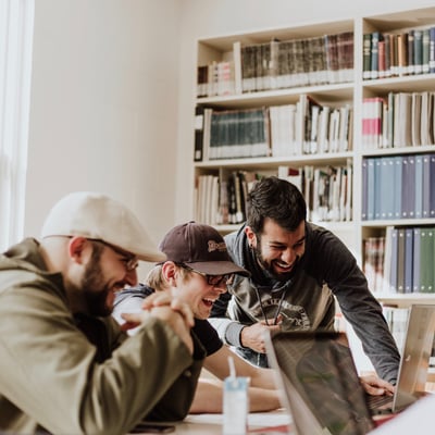 three men laughing in front of laptop
